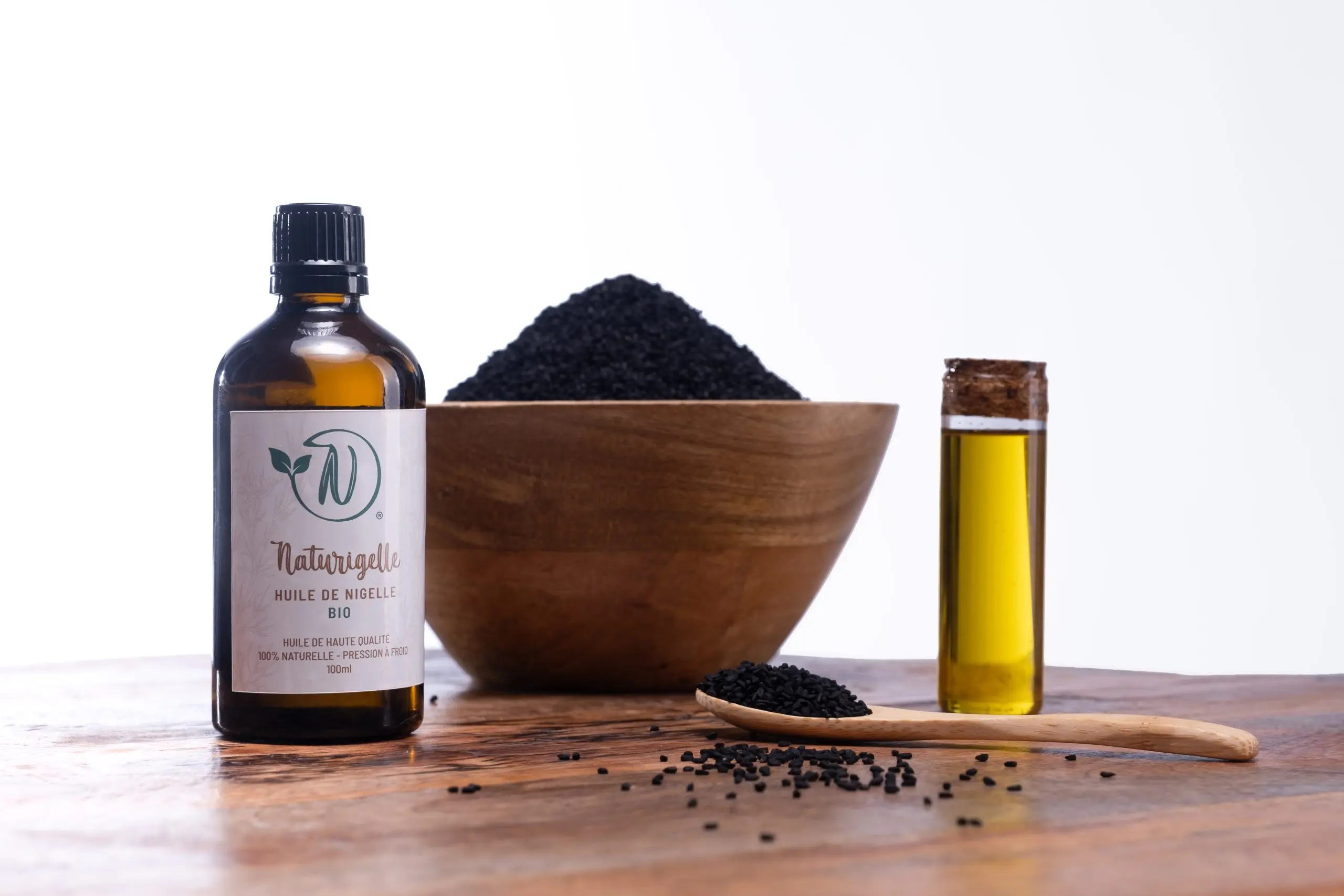 Flacon d’huile de nigelle bio Naturigelle de Naturison avec un bol de graines de nigelle et une fiole d’huile